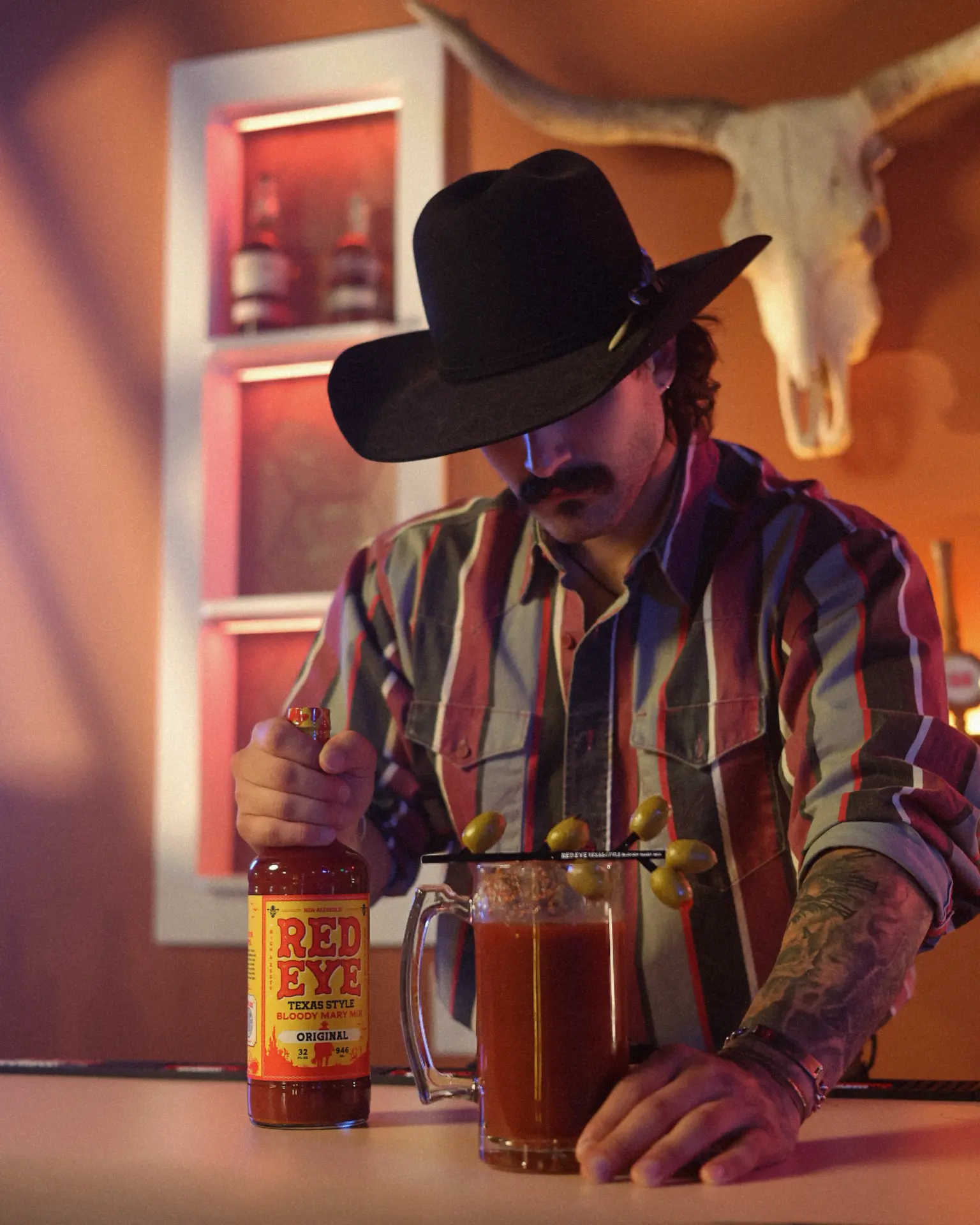 Bartender in a cowboy hat pouring Red Eye bloody mary mix into a mug of olives